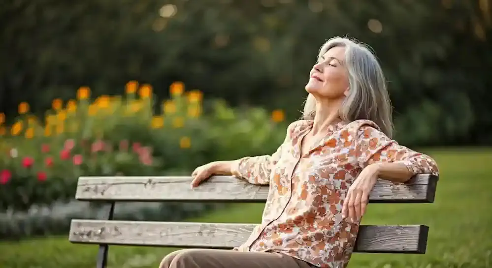A contented older woman peacefully sits on a park bench soaking up sunshine